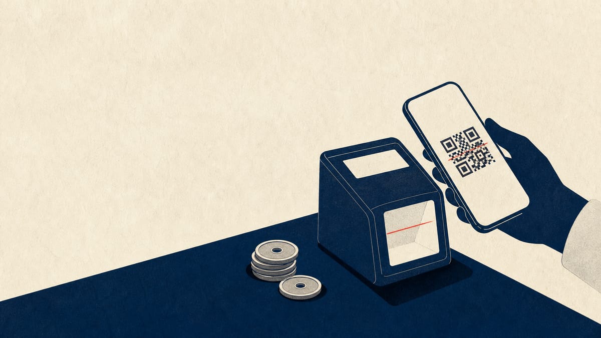 A smartphone showing a payment QR code held near a point-of-sale terminal at a convenience-store checkout counter, with a small stack of yen coins nearby.
