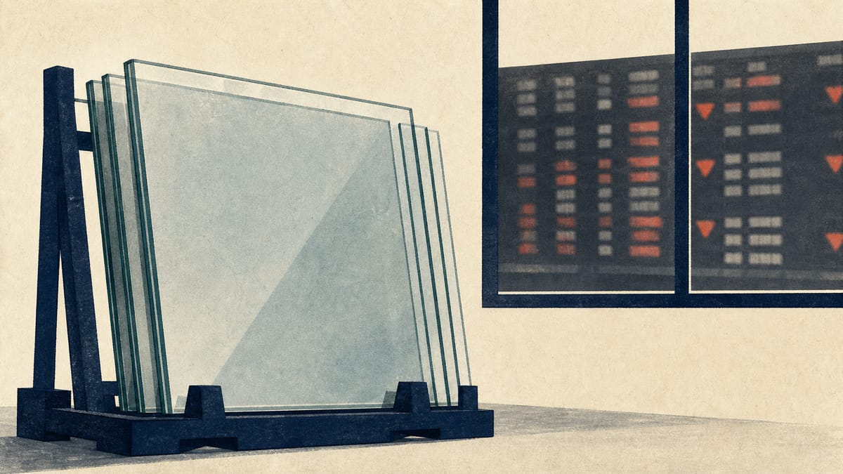Stacked industrial glass sheets in a factory setting with a blurred stock-exchange ticker board visible in the distance.